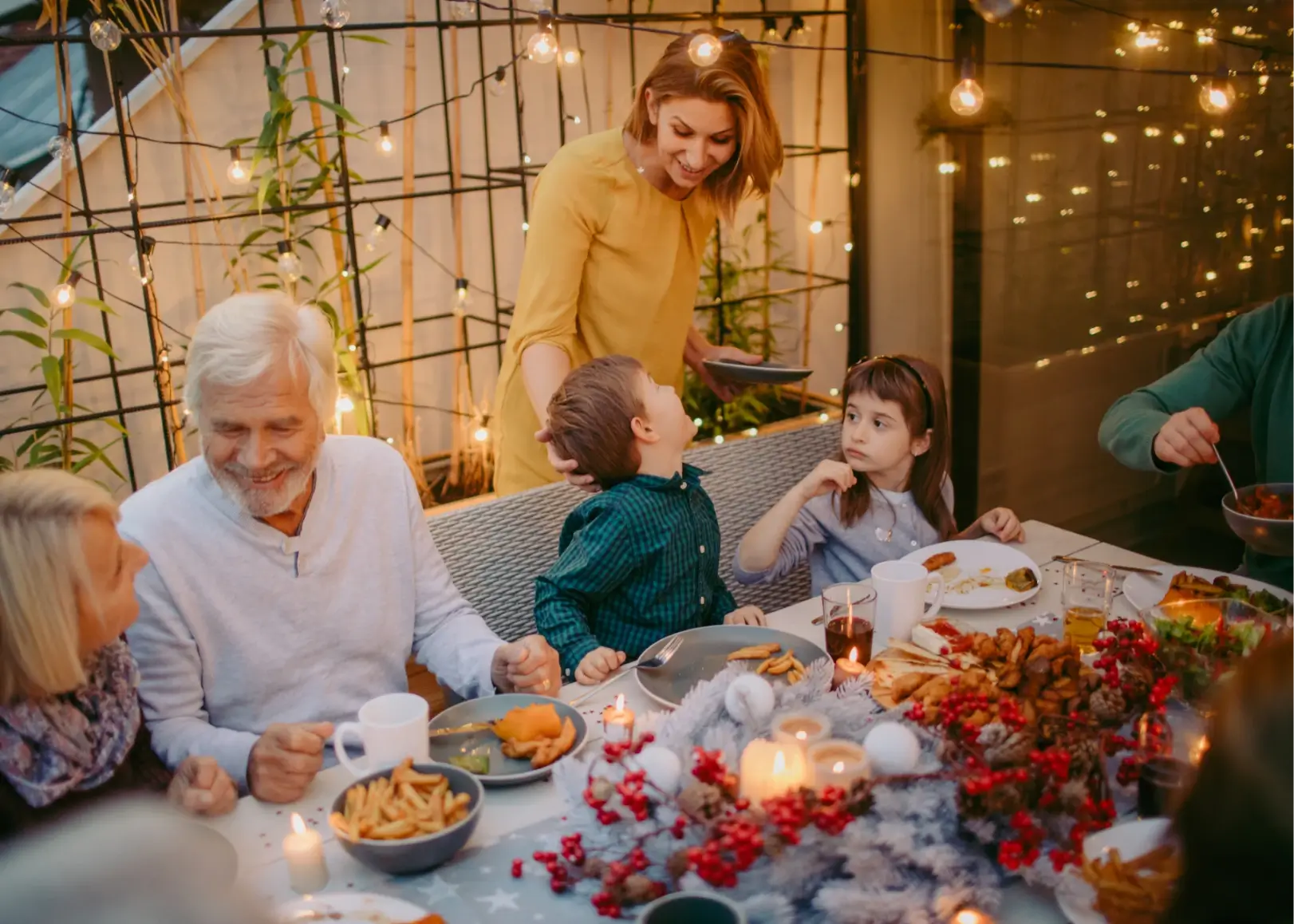 Familie genießt ein festliches Abendessen im Freien mit Lichterketten und winterlicher Dekoration.
