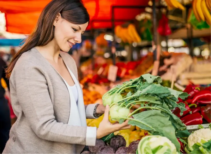 Frau kauft frisches Gemüse an einem bunten Marktstand am Wiener Naschmarkt.