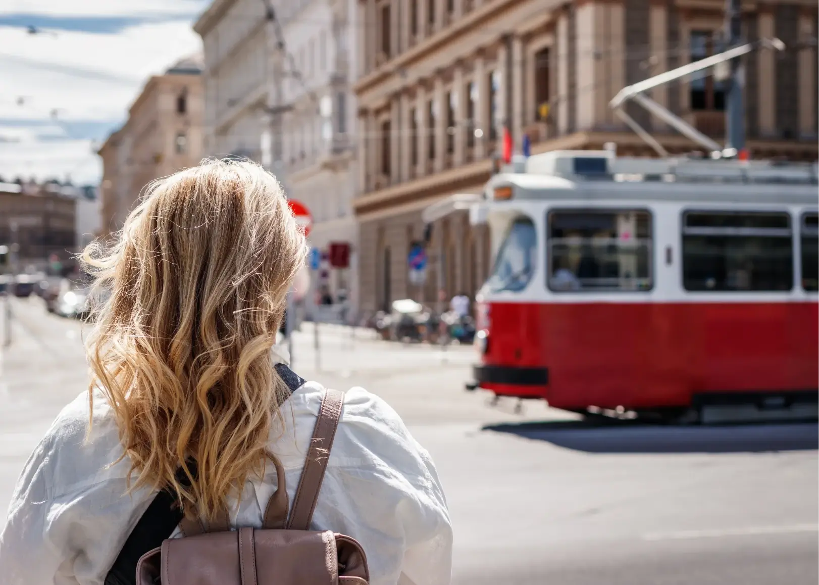 Frau mit Rucksack blickt auf eine vorbeifahrende rote Straßenbahn in der Wiener Innenstadt.