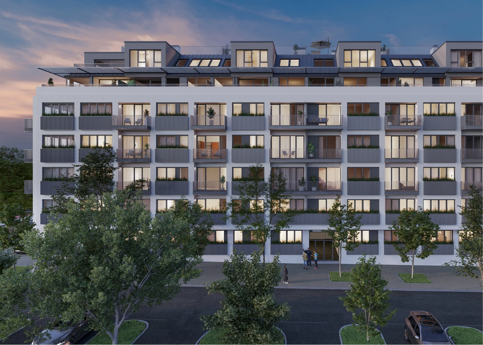 Frontalansicht eines modernen Mehrfamilienhauses mit zahlreichen Balkonen, beleuchteten Fenstern und Bäumen im Vordergrund während der blauen Stunde.